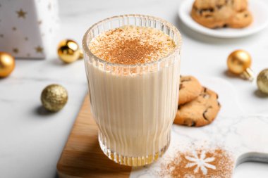 Glass of delicious eggnog with cinnamon on white table, closeup