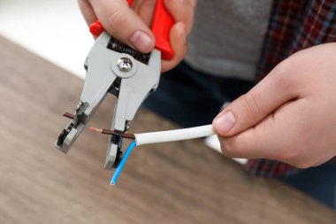Professional electrician stripping wiring at wooden table, closeup