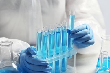 Bilim adamı açık mavi sıvıyla test tüpü alıyor, yakın plan.