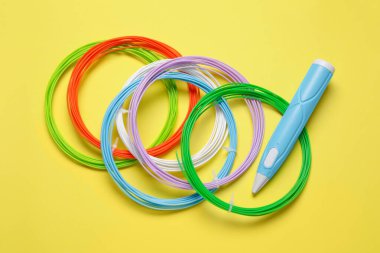 3D kalem ve sarı arkaplanda renkli plastik filamanlar, düz yatış