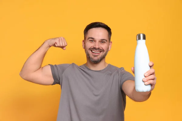 Ευτυχισμένος Άνθρωπος Κρατώντας Θερμοφόρα Μπουκάλι Και Δείχνει Χέρι Πορτοκαλί Φόντο — Φωτογραφία Αρχείου
