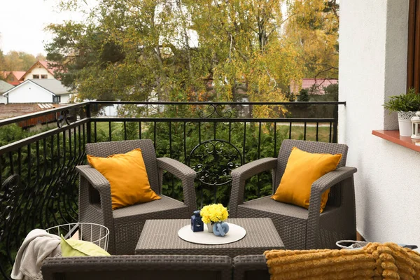 Colorful pillows, soft blanket and yellow chrysanthemum flowers on rattan garden furniture outdoors