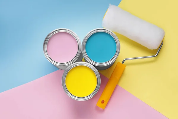 Cans with different paints and roller on color background, flat lay