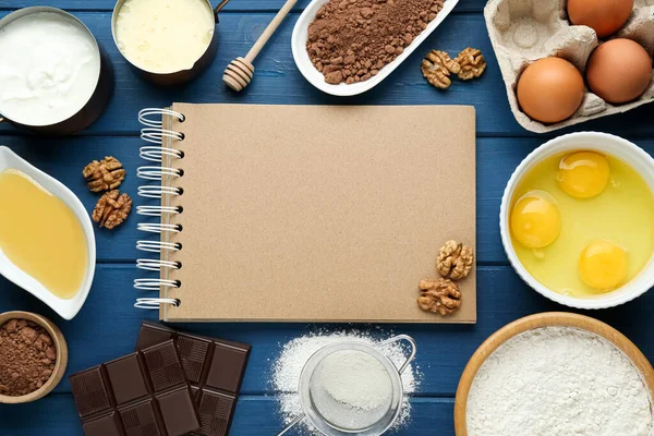 stock image Blank recipe book surrounded by different ingredients on blue wooden table, flat lay. Space for text