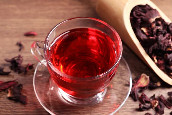 stock image Cup of fresh hibiscus tea and dry flower leaves on wooden table, closeup