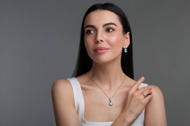 Koyu gri arka planda zarif mücevherleri olan güzel bir genç kadın.