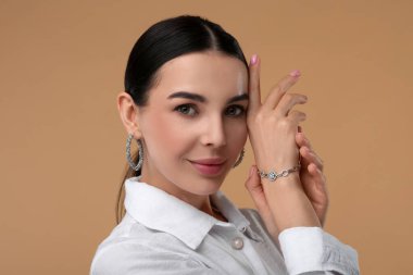Bej arka planda zarif mücevherleri olan genç bir kadın.