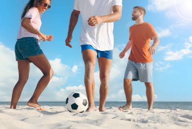 Mutlu arkadaşlar güneşli bir günde plajda futbol oynuyorlar. Düşük açı.