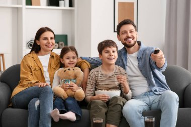Evde televizyon izleyen mutlu bir aile. Babam uzaktan kumandayla kanal değiştiriyor.
