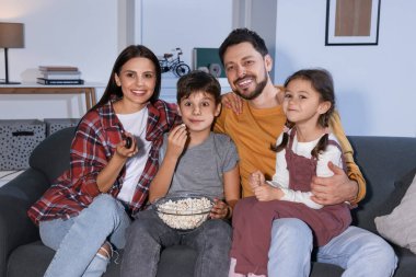 Akşamları evde film izleyen bir aile. Annem uzaktan kumandayla televizyon kanallarını değiştiriyor.