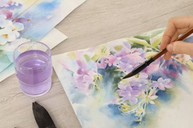 Beyaz ahşap masada suluboya çiçekleri boyayan kadın, yakın plan. Yaratıcı sanat eserleri
