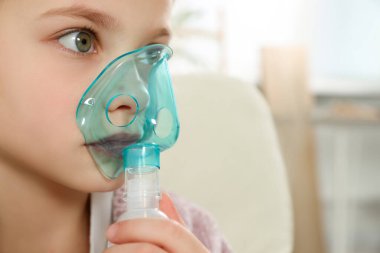 Little girl using nebulizer for inhalation indoors, closeup