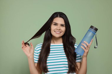 Yeşil arka planda bir şişe suyu olan genç bir kadın.