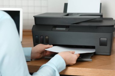 Woman loading paper into printer at wooden table indoors, closeup
