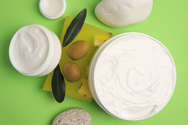Açık yeşil zemin üzerinde zeytin ve taşlar ile farklı kozmetik ürünleri, düz yatıyordu