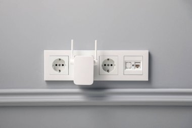 Wireless Wi-Fi repeater on light grey wall clipart