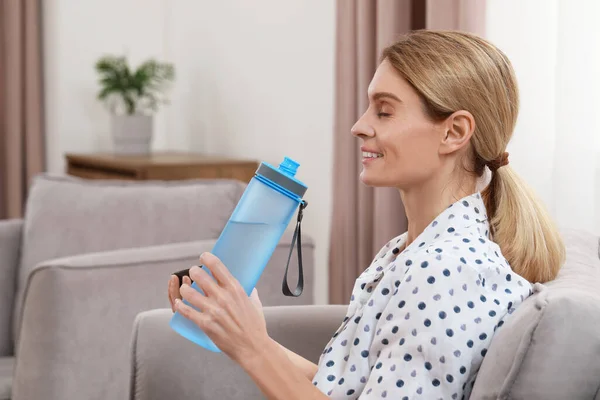 自宅のアームチェアに水のボトルを持つ女性 — ストック写真