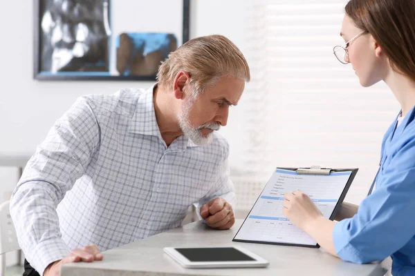 Doctor showing medical card to patient at table in clinic