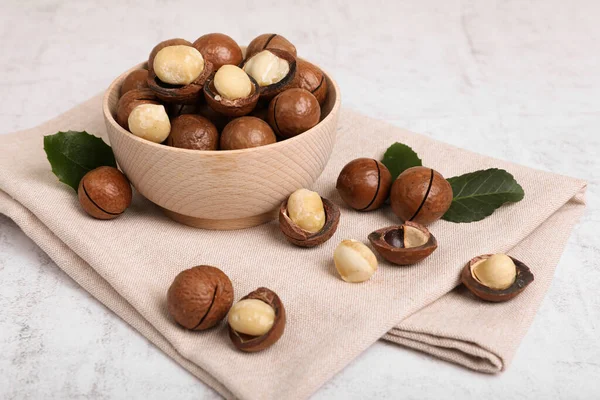 stock image Bowl with organic Macadamia nuts and green leaves on white textured table