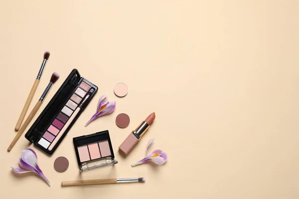 Flat lay composition with different makeup products and beautiful flowers on beige background. Space for text