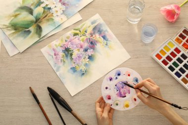 Beyaz ahşap masada suluboya çiçekleri boyayan bir kadın. Yaratıcı sanat eserleri