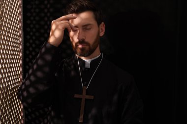 Günah çıkarma kabininde haç çıkaran cüppeli Katolik bir rahip.