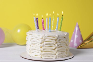 Yanan mumlarla nefis bir pasta ve beyaz ahşap masada şenlikli bir dekor.