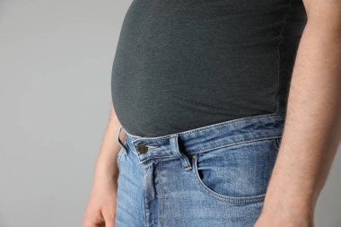 Dar tişörtlü şişman bir adam ve açık gri arka planda kot pantolon, yakın plan. Metin için boşluk