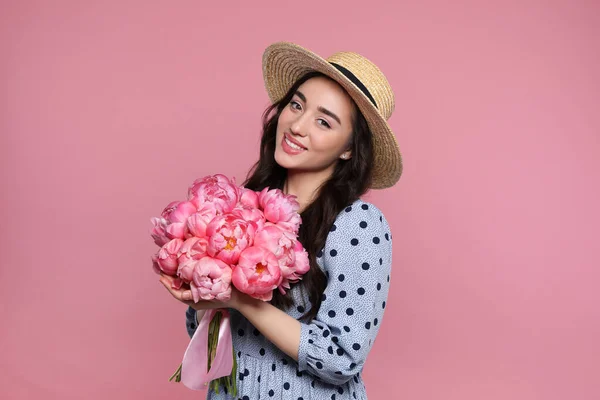 美しいです若いです女性でわら帽子で牡丹の花束でピンクの背景 — ストック写真
