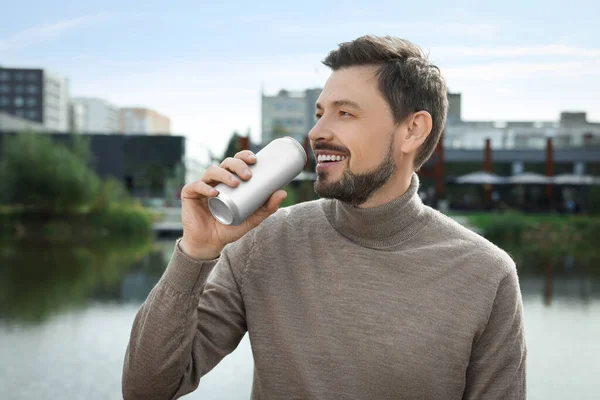 Handsome man drinking from tin can near river outdoors