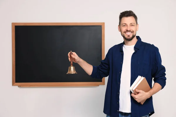 Teacher with school bell near black chalkboard indoors. Space for text