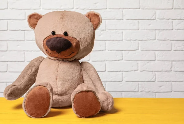 Cute teddy bear on yellow wooden table near white brick wall, space for text