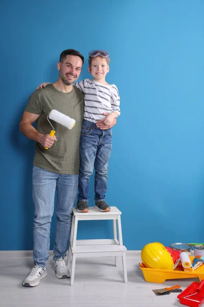 Father and son with roller near blue wall. Repair work