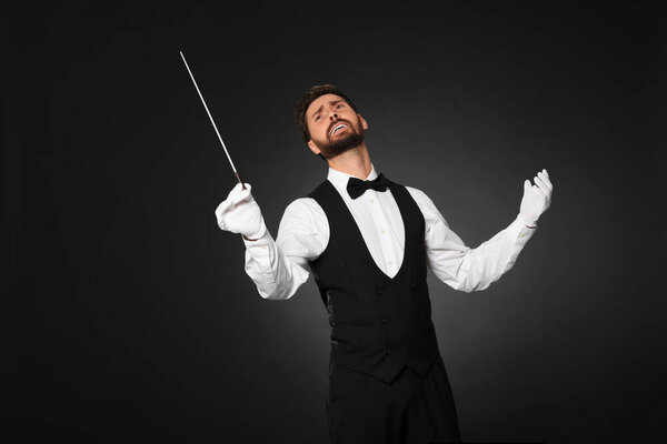 Professional conductor with baton on black background