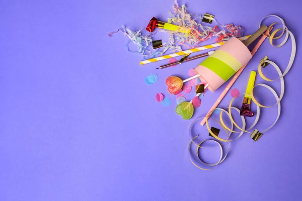 Party popper, lollipops and festive decor on violet background, flat lay