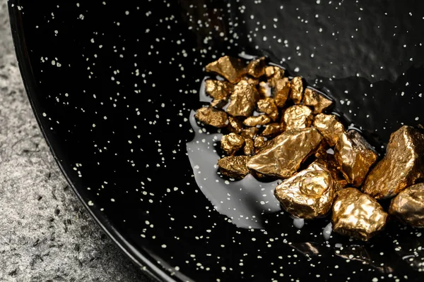 Bowl with gold nuggets on grey table, closeup