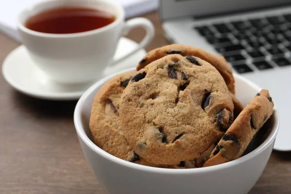 ノートパソコンの近くのチョコレートチップクッキーとテーブルの上のお茶のカップ クローズアップ — ストック写真