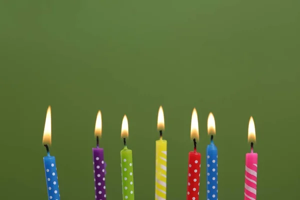 Many burning candles on green background, closeup. Birthday celebration