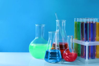 Açık mavi arka planda beyaz masadaki renkli sıvılarla farklı laboratuvar vitrinleri.