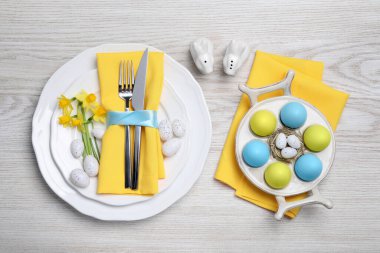Beyaz ahşap arka planda boyalı yumurta ve çatal bıçaklı şenlik masası. Paskalya kutlaması