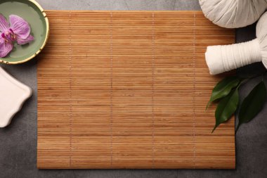 Bambu hasırlı düz kompozisyon, spa bitkisel kesesi ve gri masadaki orkide çiçekli kase. Metin için boşluk