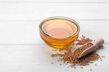 Bir kase doğal yağ ve beyaz ahşap masada hardal tohumlarıyla kepçeyle.