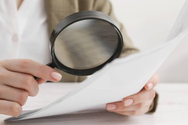 Kadın masadaki büyüteçle belgeye bakıyor, yakın plan. Konsept aranıyor