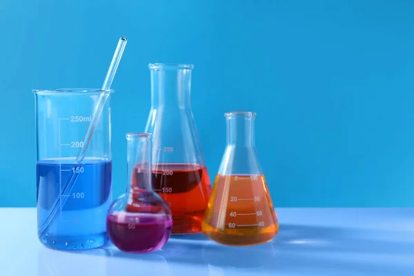不同的实验室玻璃器皿 白桌上有五颜六色的液体 背景为浅蓝色 案文的篇幅 — 图库照片