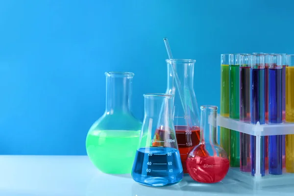 不同的实验室玻璃器皿 白桌上有五颜六色的液体 背景浅蓝色 — 图库照片