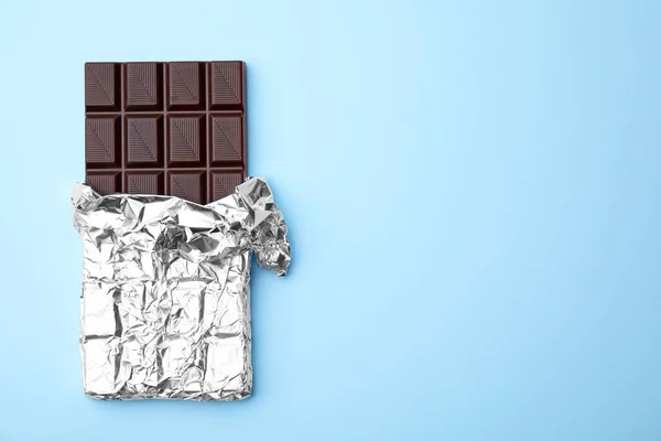 Tasty chocolate bar on light blue background, top view. Space for text
