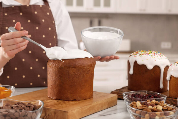 Woman decorating traditional Easter cake with glaze at white marble table in kitchen, closeup