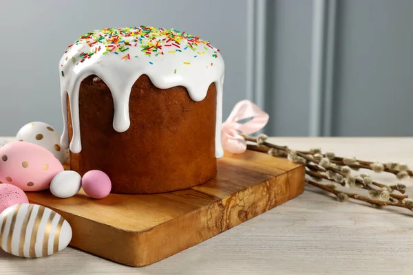 stock image Delicious Easter cake with sprinkles, decorated eggs and willow branches on white wooden table near light grey wall indoors