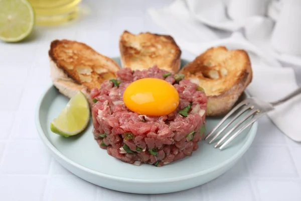 stock image Tasty beef steak tartare served with yolk, toasted bread and lime on white tiled table