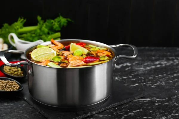 stock image Saucepan with delicious Tom Yum soup and ingredients on black marble table. Space for text